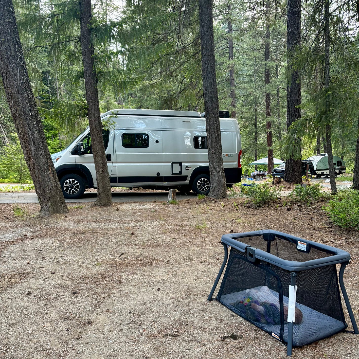 A camping van and a portable baby crib surrounded by trees