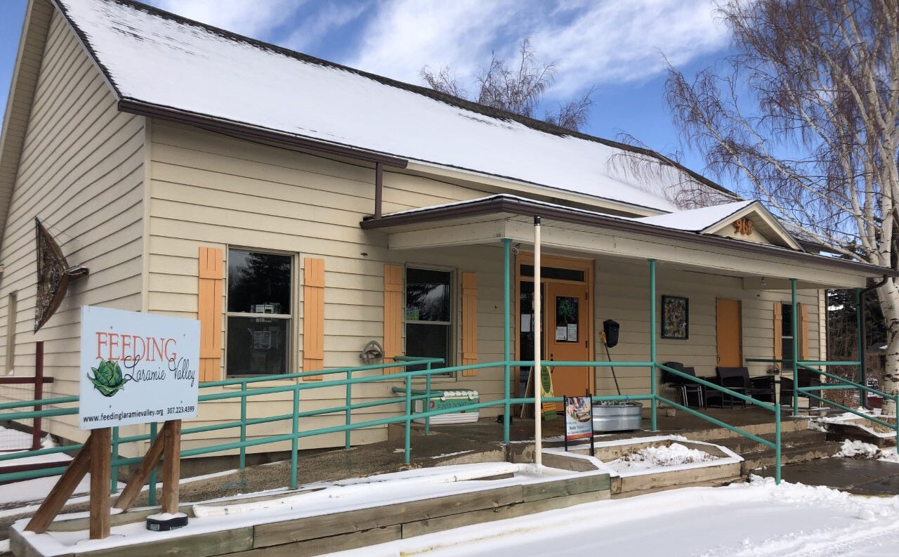Beige building with orange trim and green railings is covered with snow on an early spring day. A sign reads "Feeding Laramie Valley" Beige building with orange trim and green railings is covered with snow on an early spring day. A sign reads "Feeding Laramie Valley"