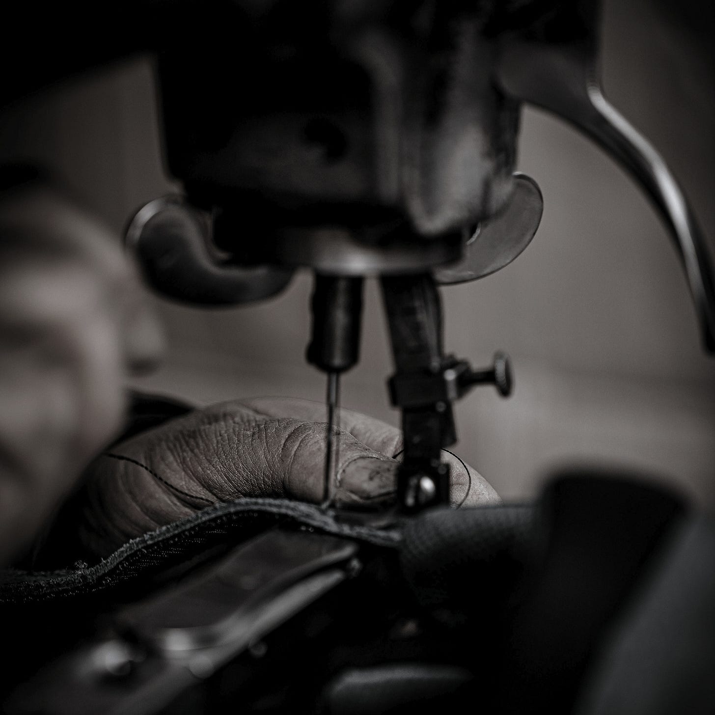 Close-up of a craftsman's hands guiding leather through a vintage sewing machine, illustrating the slow, deliberate work of traditional craftsmanship.
