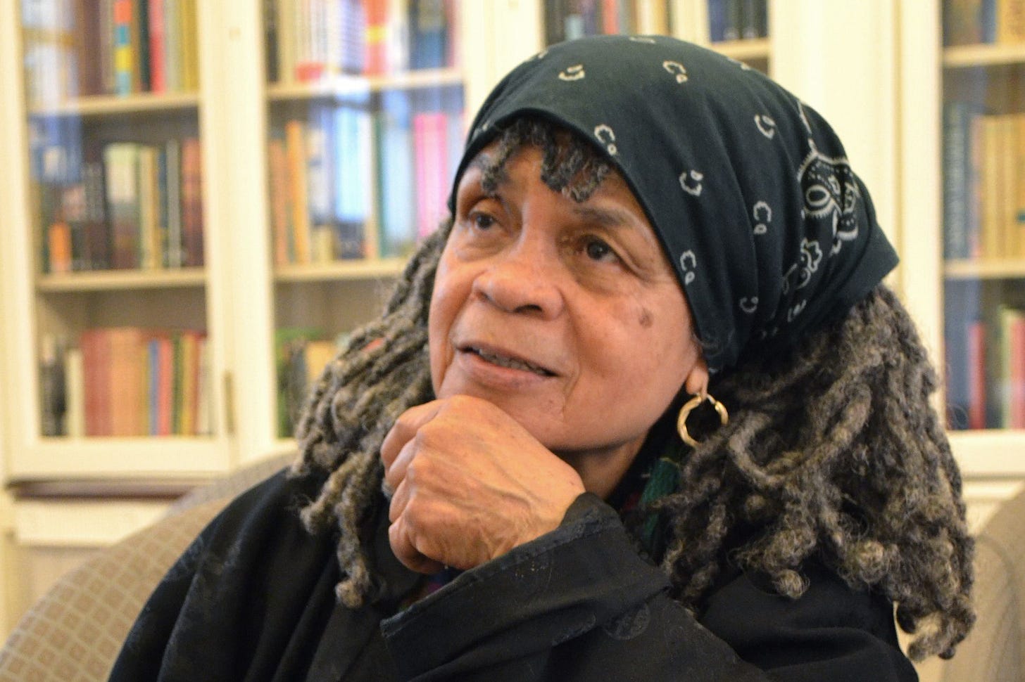 a color photograph - a headshot of Sonia Sanchez with books lining a wall behind her