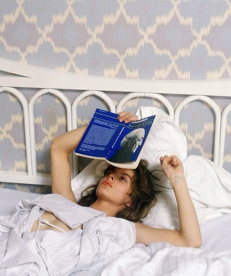 This may contain: a woman laying in bed with a book on top of her head while reading it