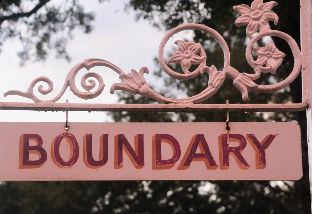 pink decorative sign that says "BOUNDARY" against a backdrop of trees