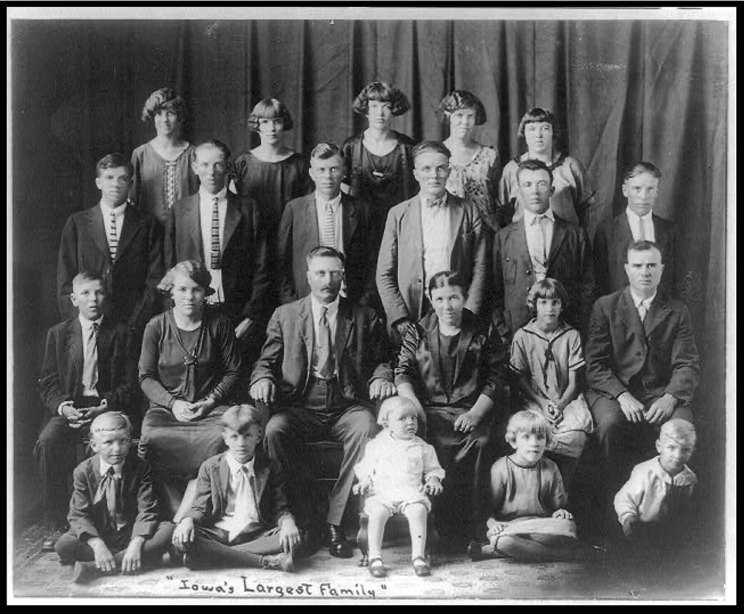 A black-and-white photo of a family of 22 members. The family is nicely-dressed; the females wear their hair in the Marcelled "bob" of the 1920s.