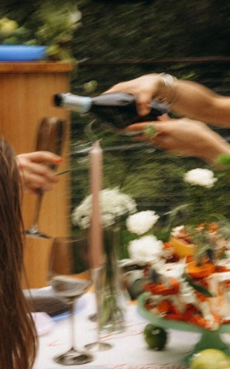This may contain: two people are pouring wine into glasses at a table with flowers and candles on it