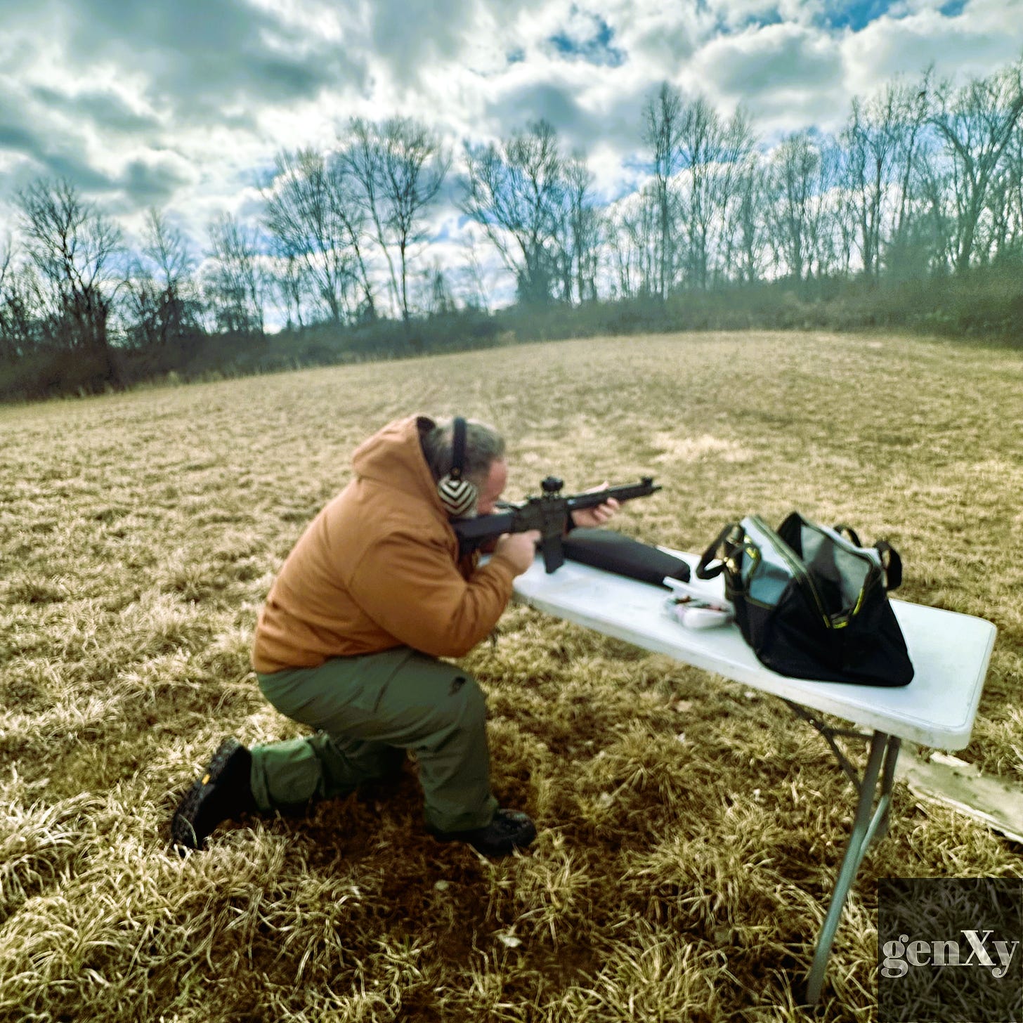 A man firing an AR-style rifle while crouched over a folding table in a winter field. A man firing an AR-style rifle while crouched over a folding table in a winter field.