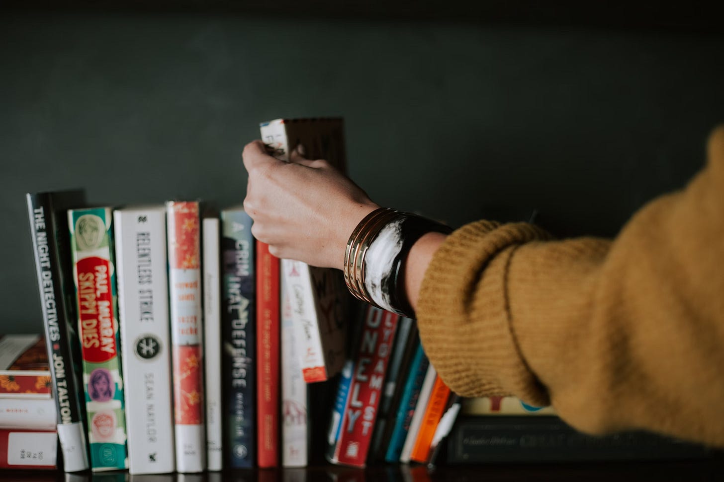 arm in yellow sweater picking a red and white book from a shelf