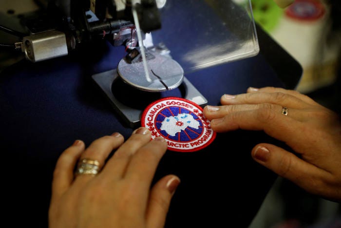 Worker sewing Canada Goose patch onto jacket.