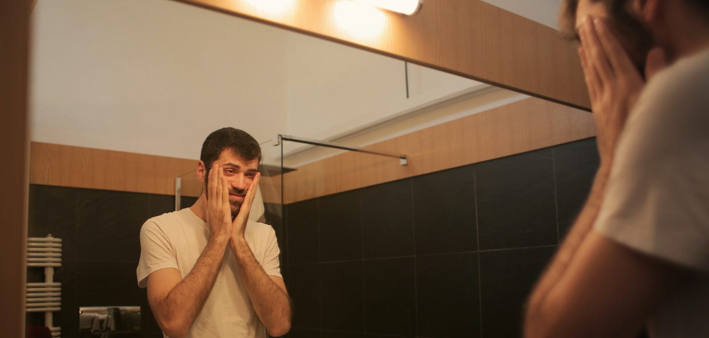 A header picture of a man looking at a mirror with his hands over his face.