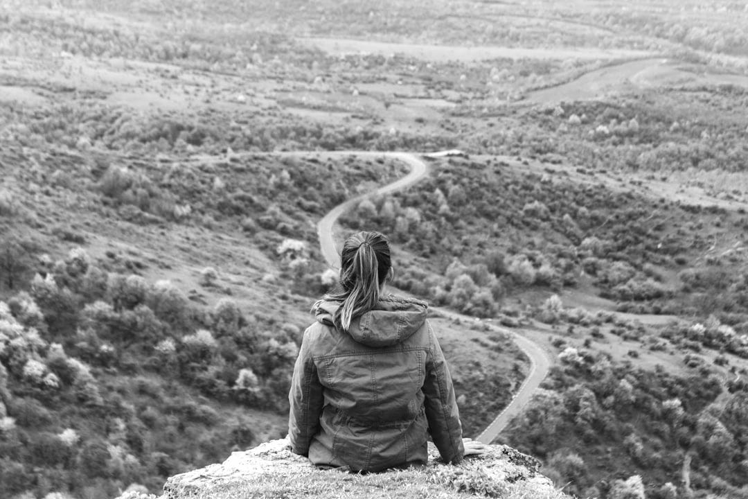 woman sitting on grey cliff woman sitting on grey cliff
