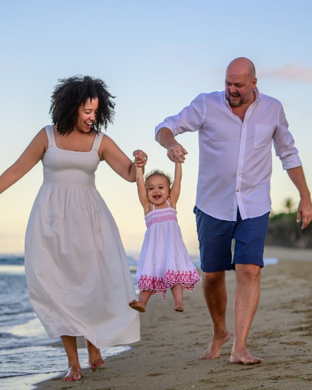 Jessica and her husband on the beaching swinging their daughter by the hands