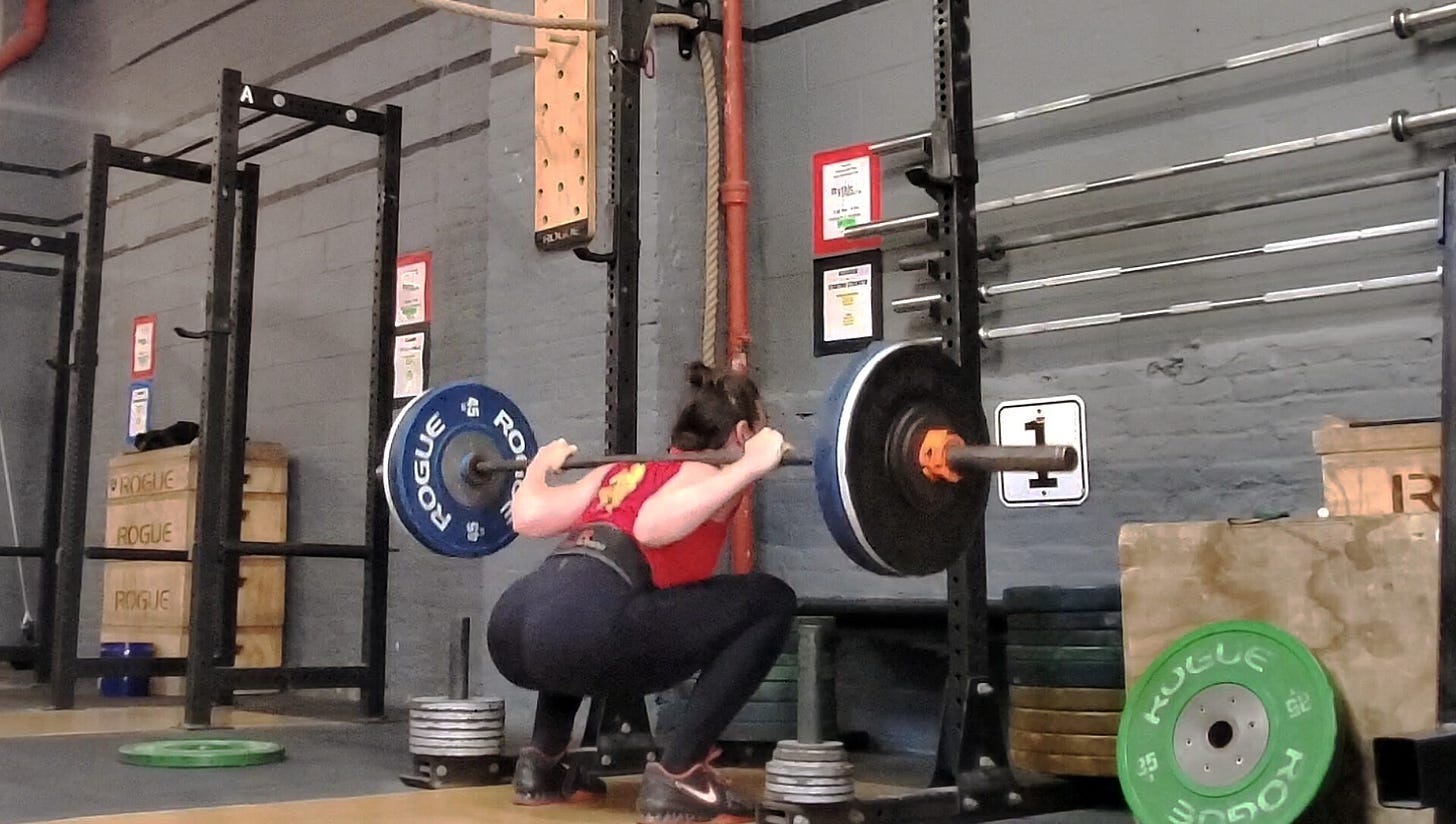 The author sitting into the bottom of a squat position with a loaded barbell across their upper back