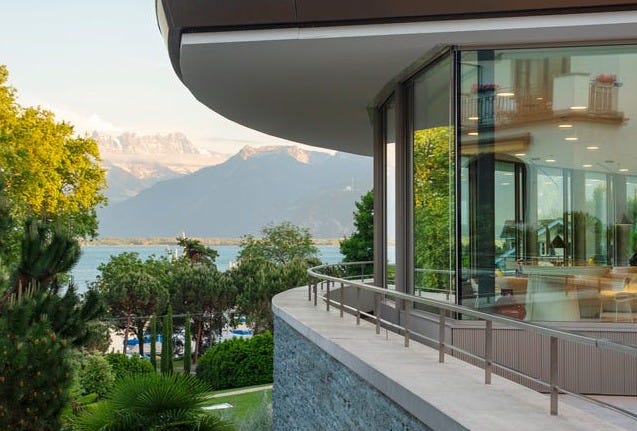 Modern building with large windows overlooking a lake and mountains.