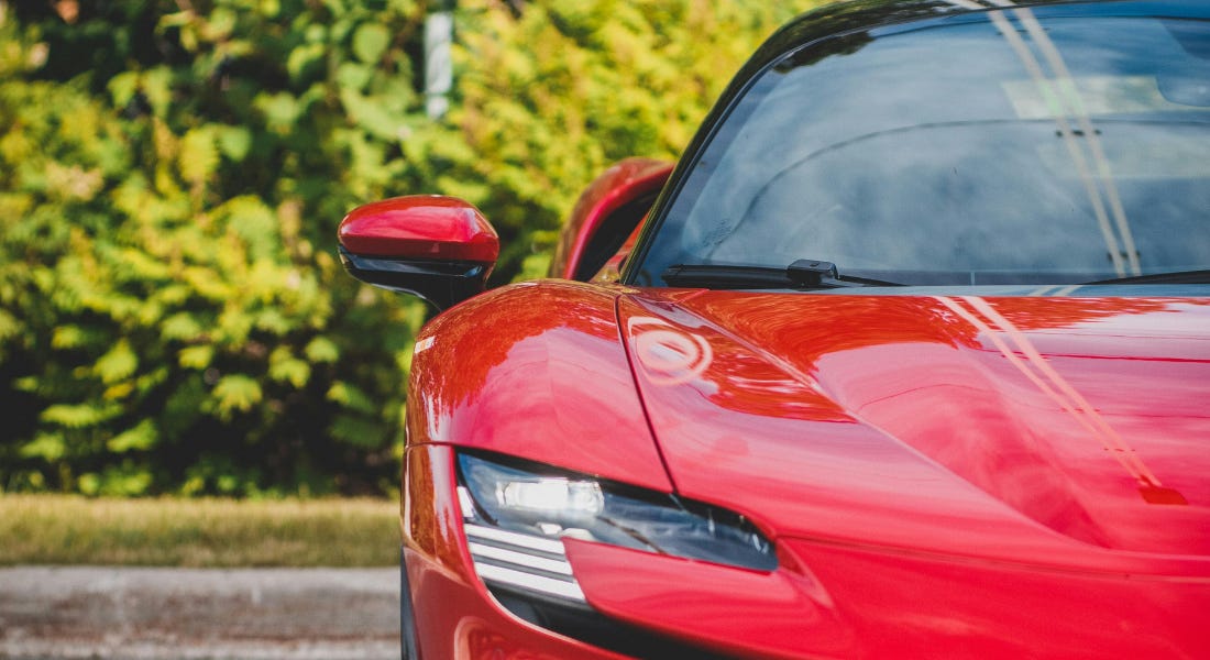 A red Ferrari parked in front of a green hedge