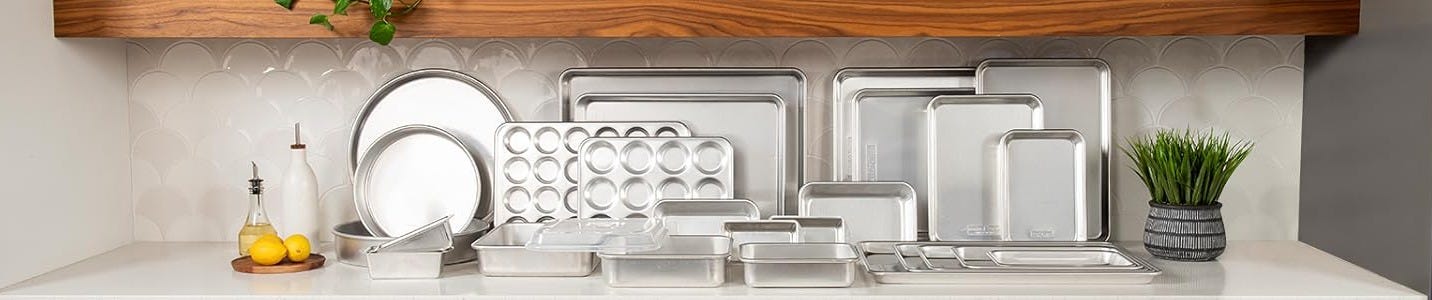 Commercial-grade aluminum sheet pan set and bakeware collection displayed on a modern kitchen counter, featuring multiple baking sheets, muffin pans, and roasting trays for meal prep, batch cooking, and home baking enthusiasts seeking durable kitchen essentials at www.AthleteMealPrep.com