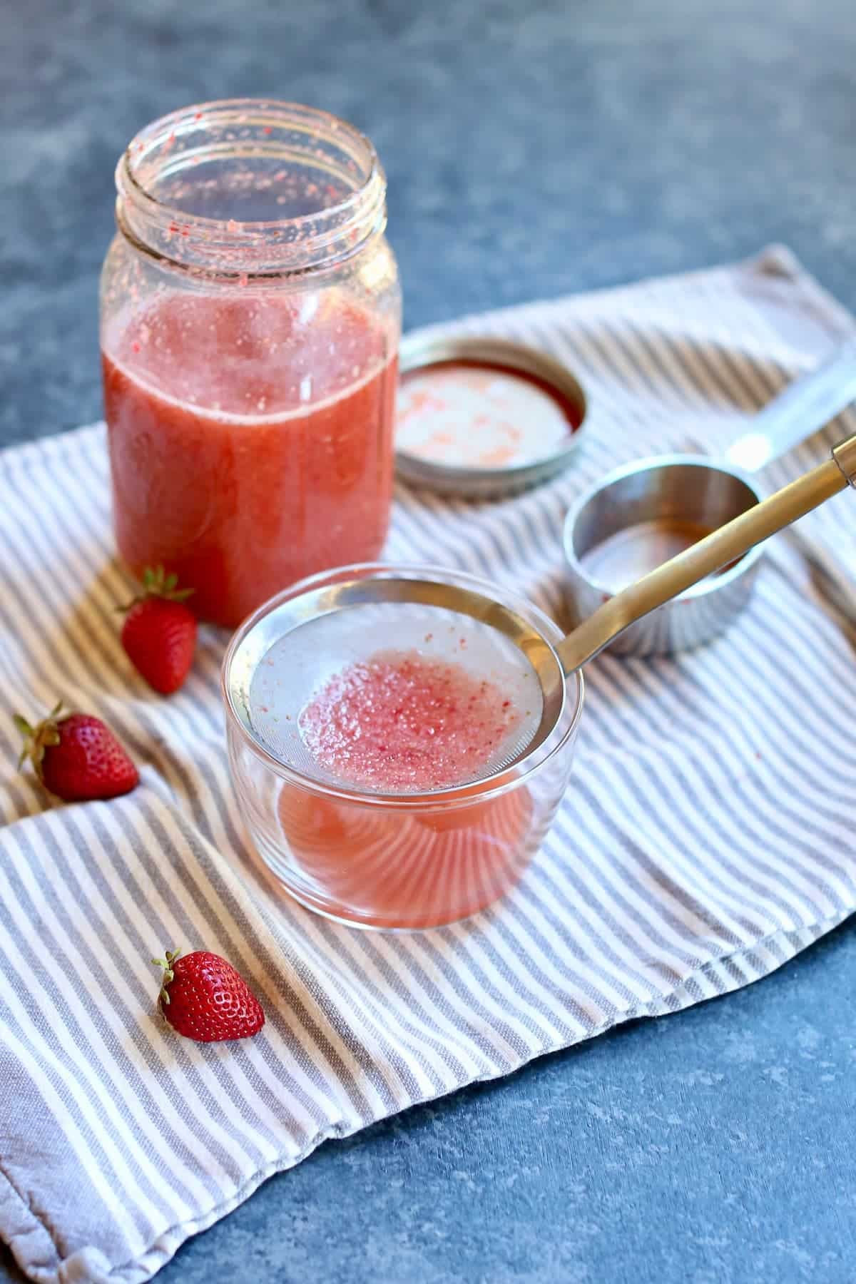 a set up of a drink being strained on into a glass bowl from a jar on a table.