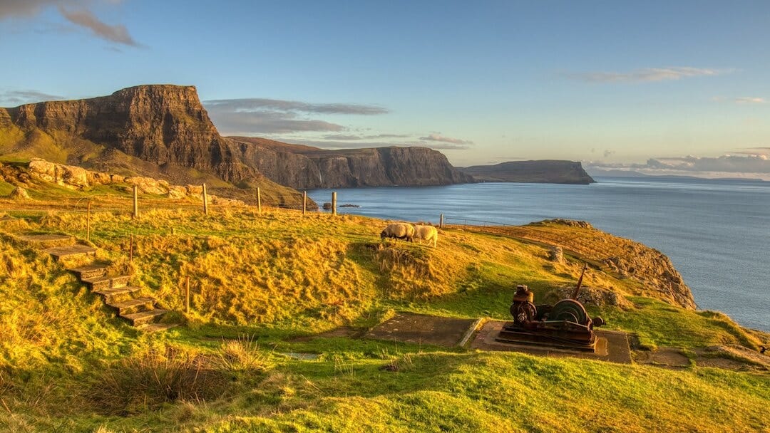 Sheep graze besides steps and an old hoist with cliffs in the background