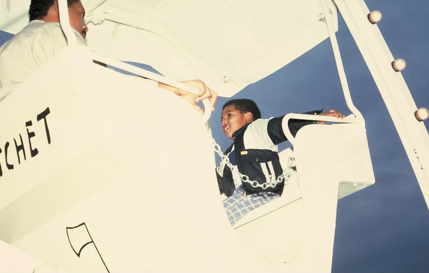 Vintage photo of a young black boy riding a white carousel painted by Basquiat.