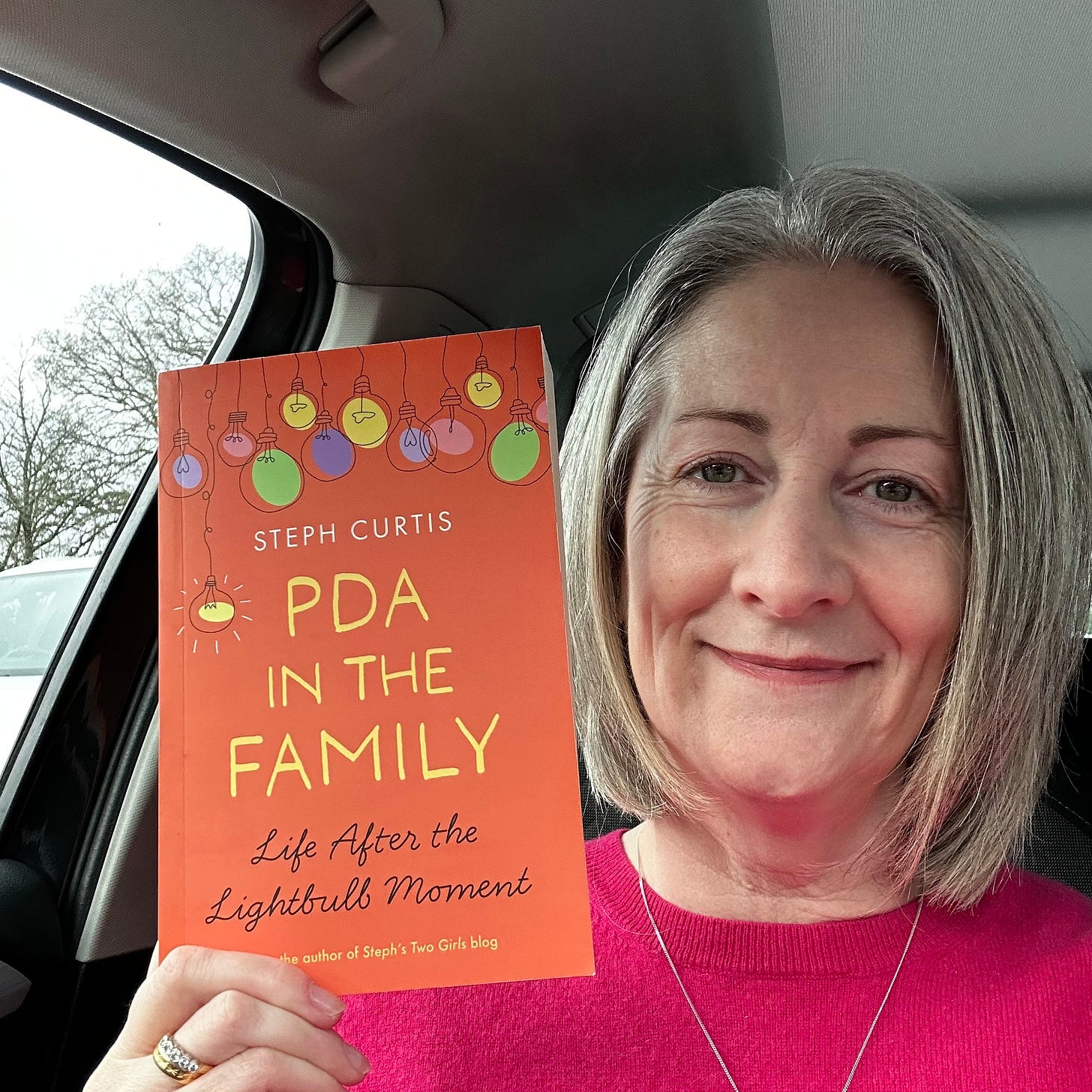 silver haired me with smile on face sitting in car holding up PDA in the Family book