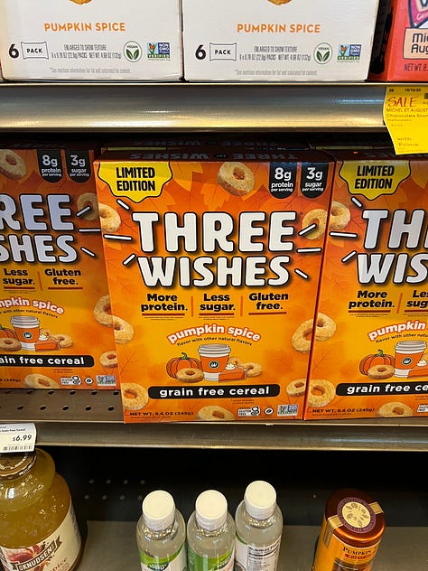 A grid of six photos of pumpkin-flavored products on shelves at an American Whole Foods: pumpkin spice grain-free cereal, pumpkin spice popcorn, pumpkin spice oat milk, cans of pumpkin chai hard tea, pumpkin spice oat bites and a pumpkin almond flour pancake mix.