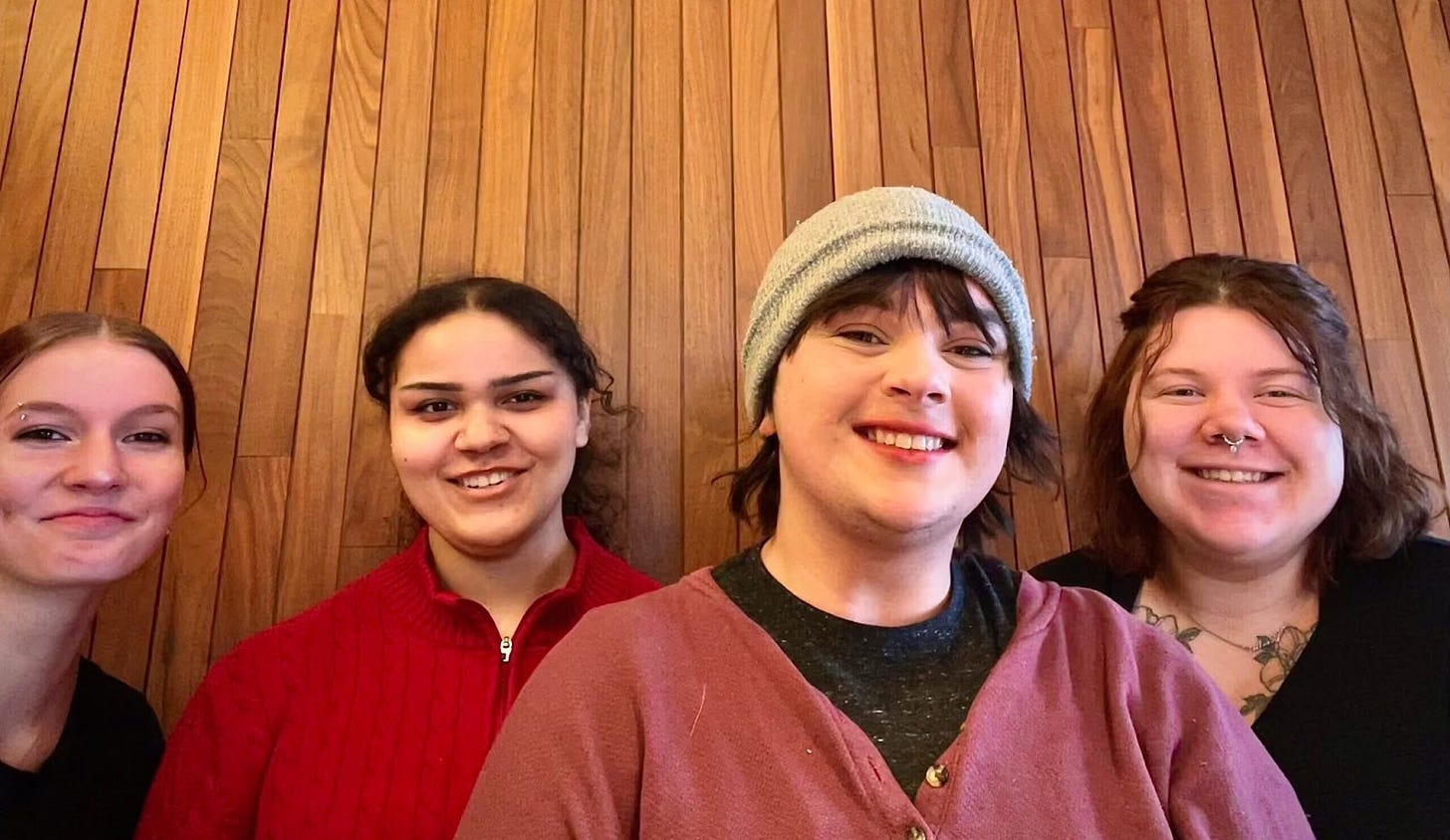 four young people with brown hair stand smiling against a wooden wall four young people with brown hair stand smiling against a wooden wall