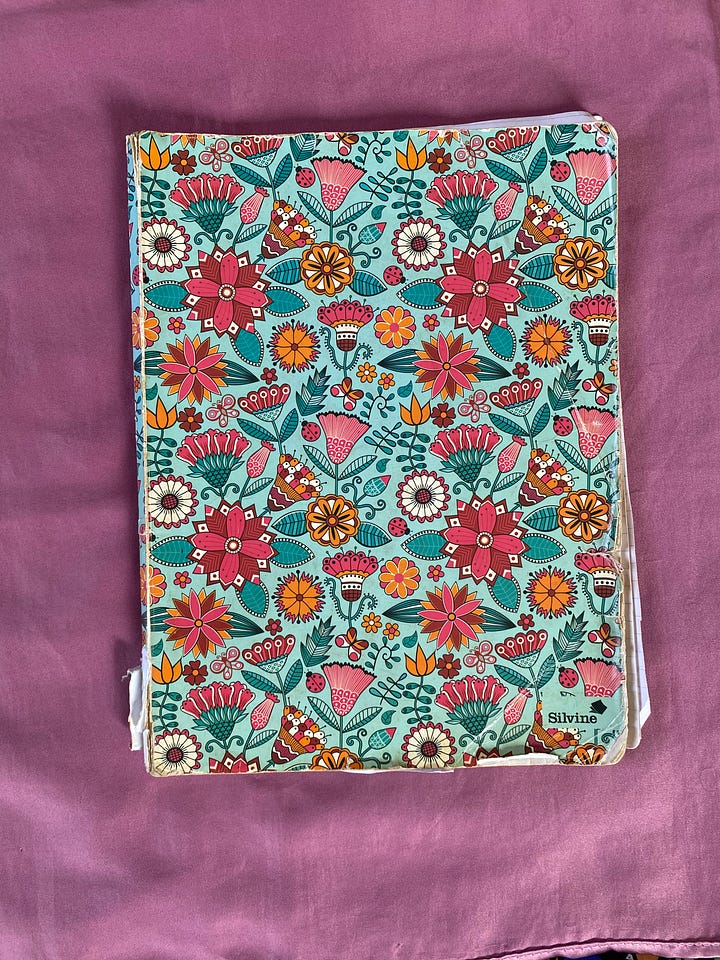 Closed notebook with colourful flora on a surface and opened notebook with scribbles and writings inside