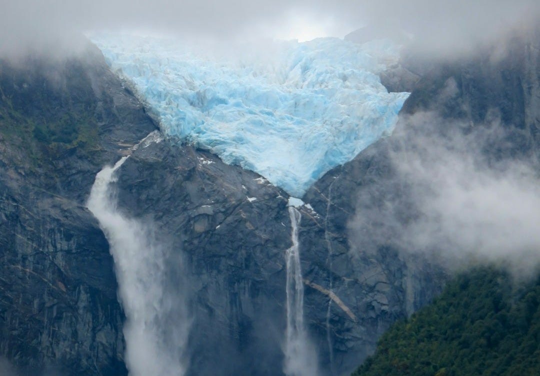 A very tall waterfall with a big blue glacier in the background A very tall waterfall with a big blue glacier in the background