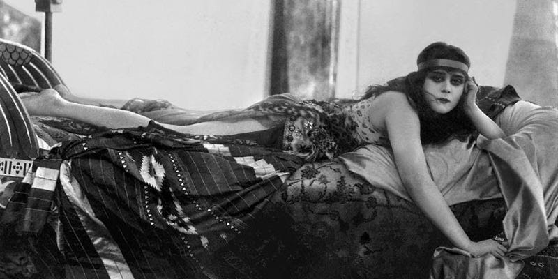 Publicity photo of Theda Bara in “exotic” garb sprawled decadently on a chaise longue.