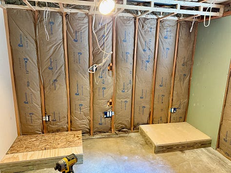 Three photos of a basement renovation in progress. The first shows plumbing pipes set in fresh concrete, the second shows an insulated orange pipe, and the third shows a framed wall with insulation and electrical wiring installed.