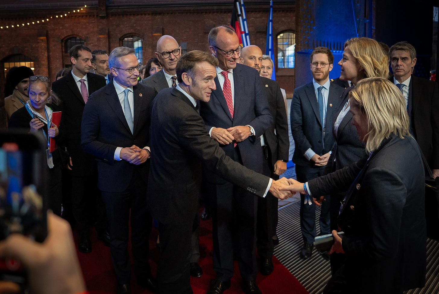 © BMDS / Woithe. EU-Vizepräsidentin Henna Virkkunen begrüßt Bundeskanzler Friedrich Merz und den französischen Präsidenten Emmanuel Macron. Im Hintergrund sind Bundesdigitalminister Karsten Wildberger und sein französischer Amtskollege Roland Lescure zu sehen.