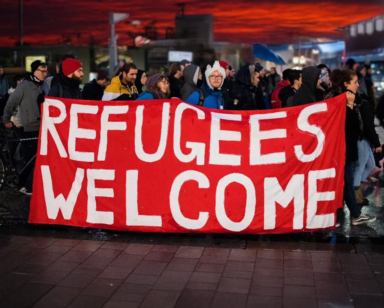 Groep mensen met spandoek ‘Refugees Welcome’ tijdens demonstratie bij zonsondergang Groep mensen met spandoek ‘Refugees Welcome’ tijdens demonstratie bij zonsondergang