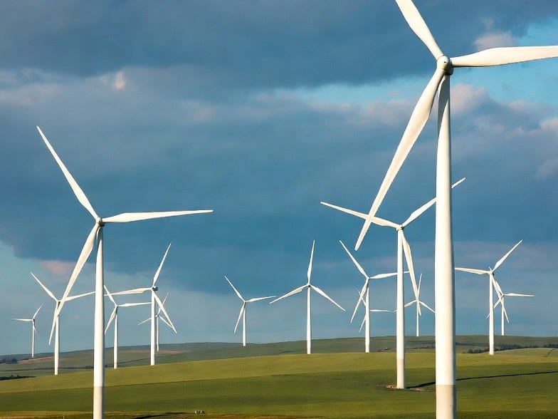 A photograph of a wind farm in a rural landscape with turbines on rolling green hills under a partly cloudy sky. A photograph of a wind farm in a rural landscape with turbines on rolling green hills under a partly cloudy sky.