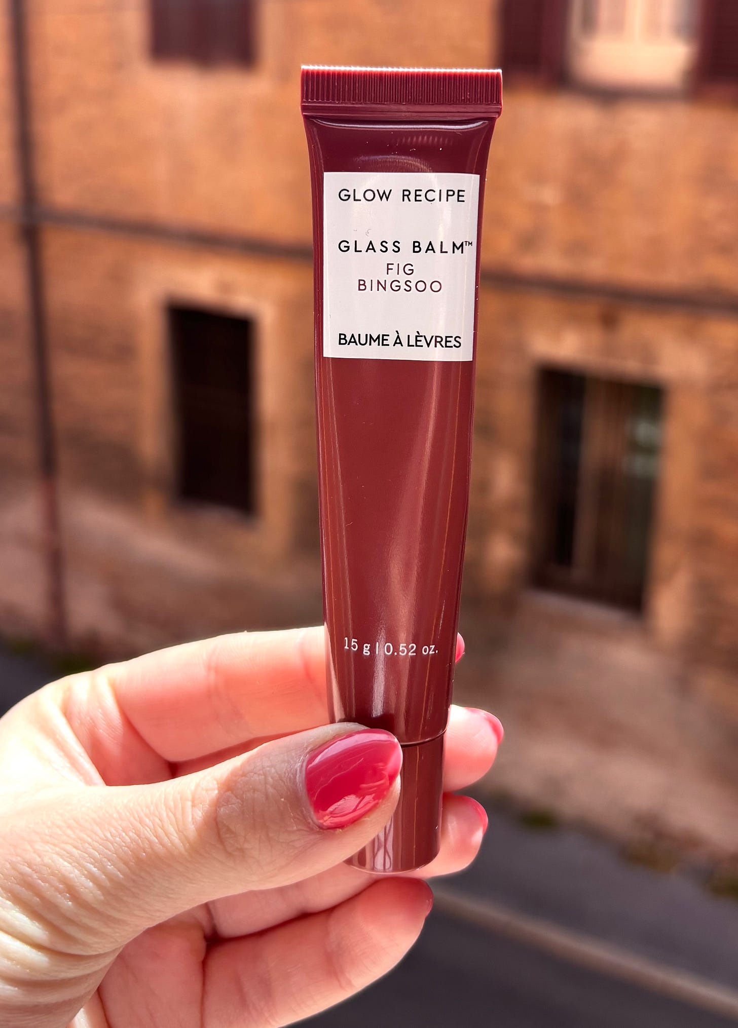 Close-up shot of Glow Recipe Glass Balm in the shade Fig Bingsoo, a mauve lip treatment tube held in hand.