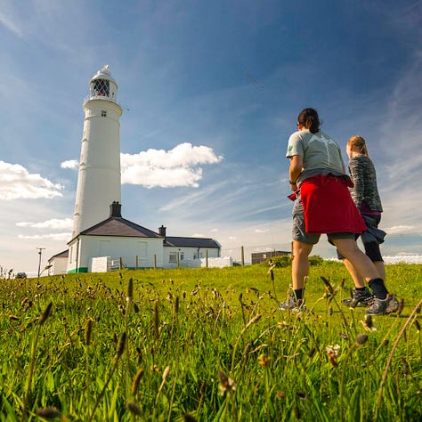 A gallery of three photographs showing different Welsh lighthouses. From left to right: the stark white tower of Nash Point standing on a green clifftop; the red and white striped Point of Ayr lighthouse resting on a sandy beach at sunset; and the rustic, cast-iron Whiteford Point lighthouse surrounded by expansive tidal flats.