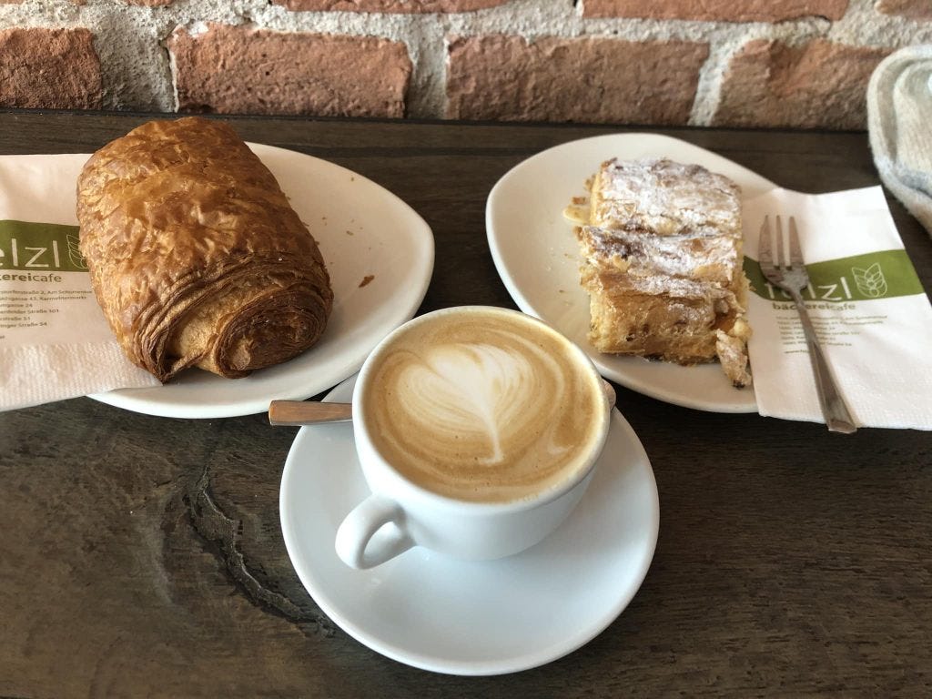 A chocolate-filled croissant and a peach filled pastry sitting next to an espresso with a foamed milk decoration on top. A chocolate-filled croissant and a peach filled pastry sitting next to an espresso with a foamed milk decoration on top.