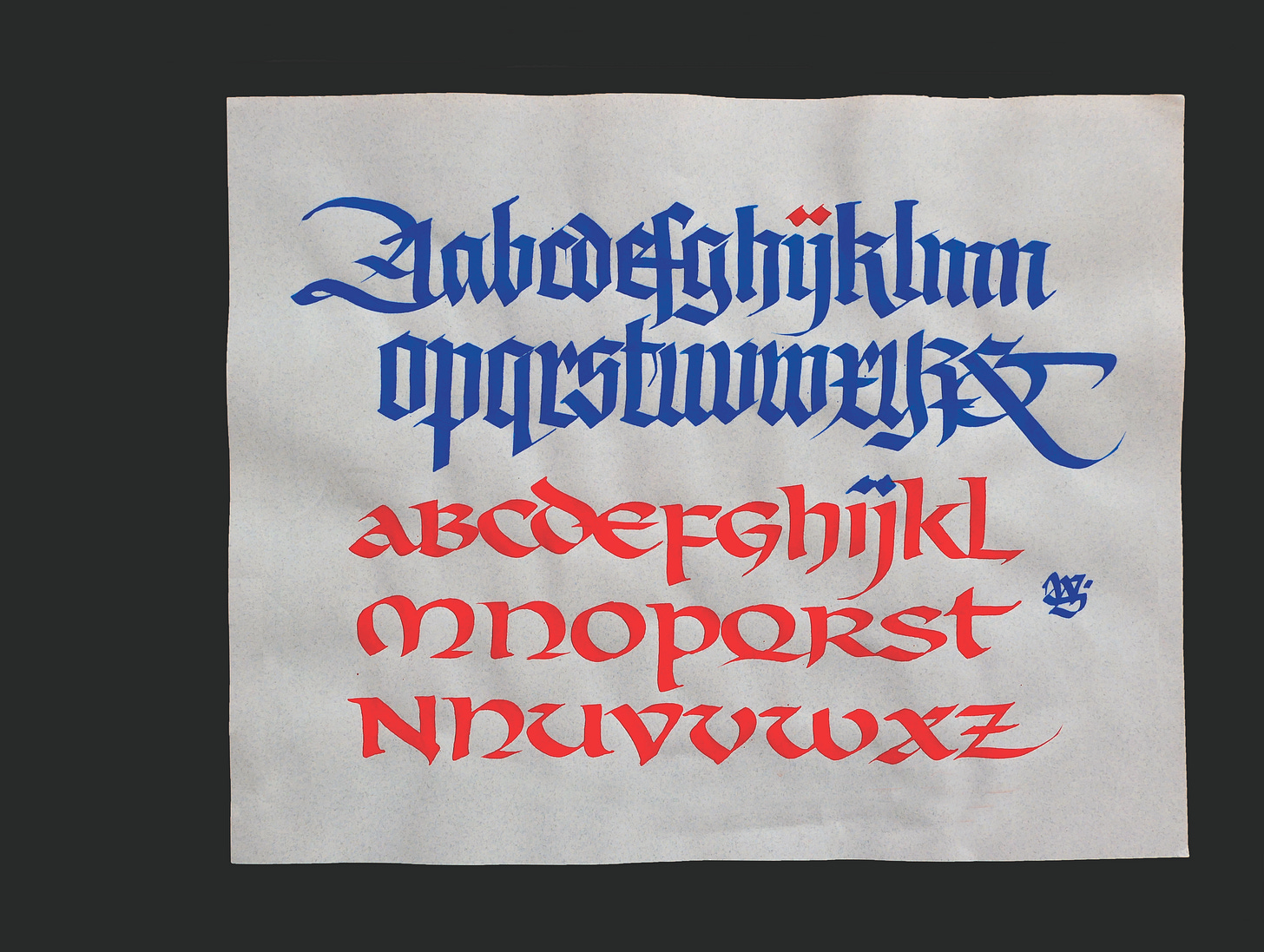 Calligraphy alphabet sampler featuring blue blackletter script and red uncial script on parchment-style paper.