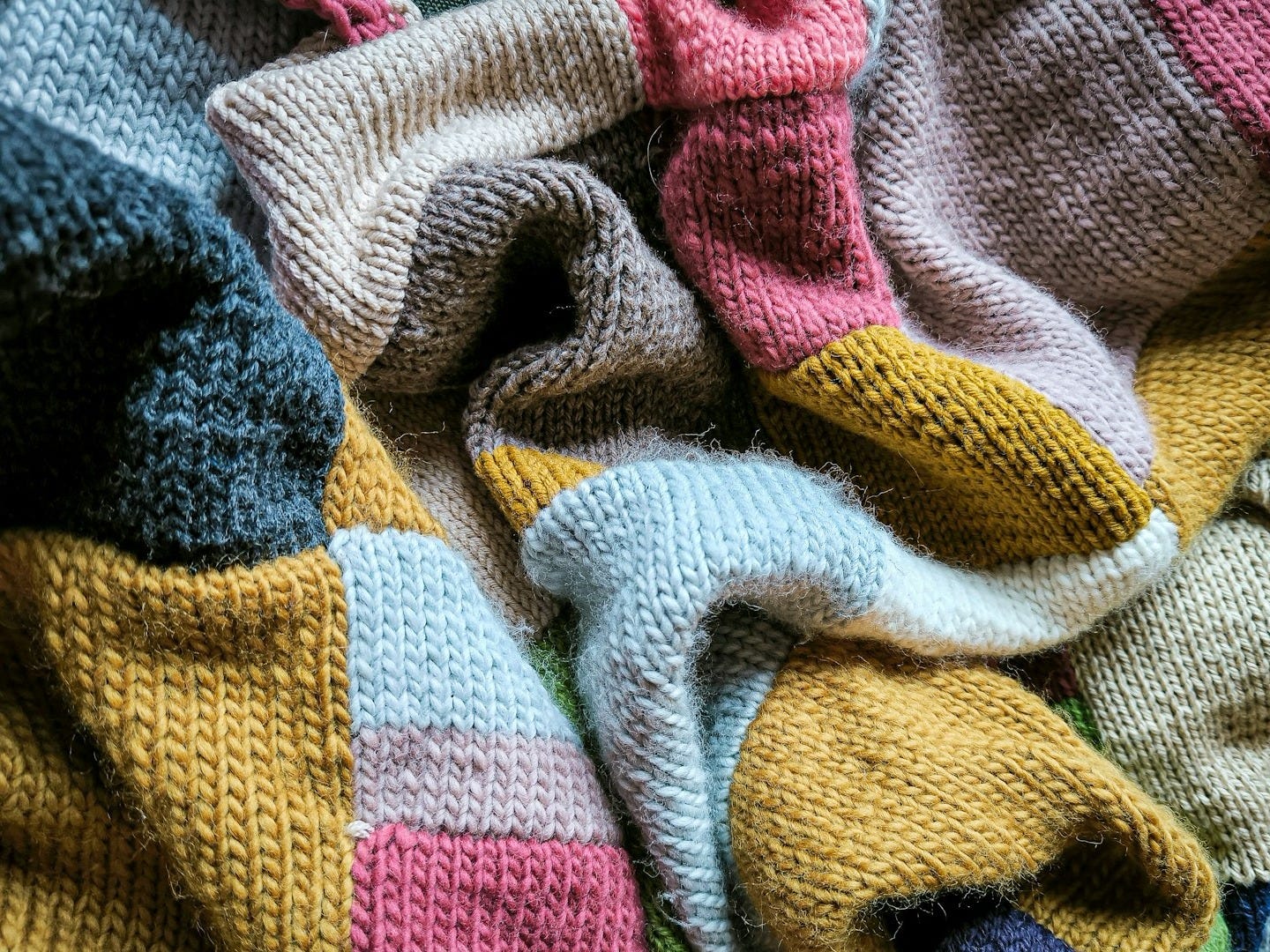 a knitted teddy bear laying on top of a blanket a knitted teddy bear laying on top of a blanket