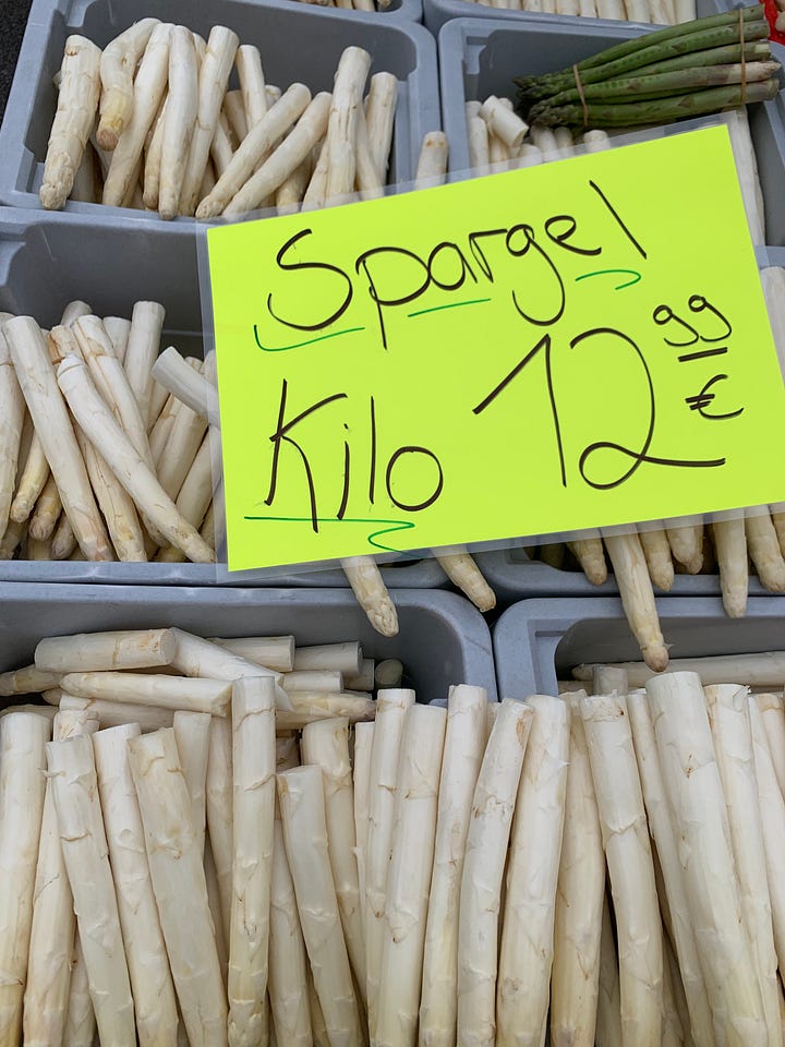 top left to bottom right: image of two spring raspberry colored cocktails with olives and a thick tubular pasta "straw", containers of white asparagus for sale at 12.99Euro per kilo, barlauch gnocchi (green)with price, cheerful red Karl'sStrawberries kiosk