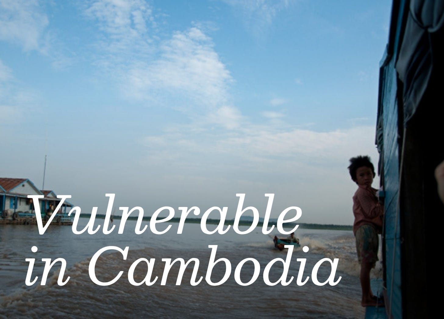 Child standing on the side of a wooden boat plying a river in Cambodia. Bright blue sky in the background. Child standing on the side of a wooden boat plying a river in Cambodia. Bright blue sky in the background.