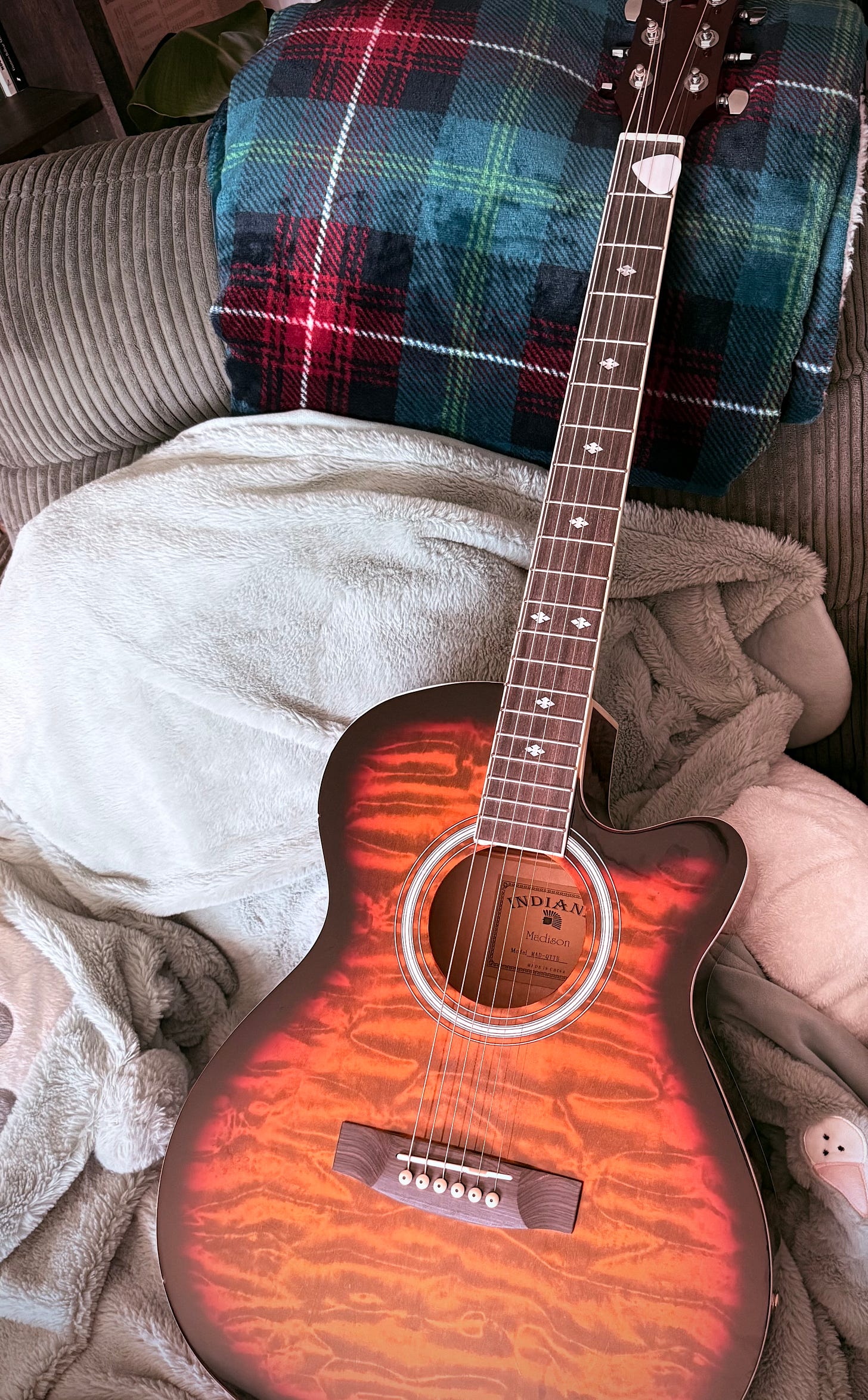 An acoustic guitar resting in a warm, cozy room.