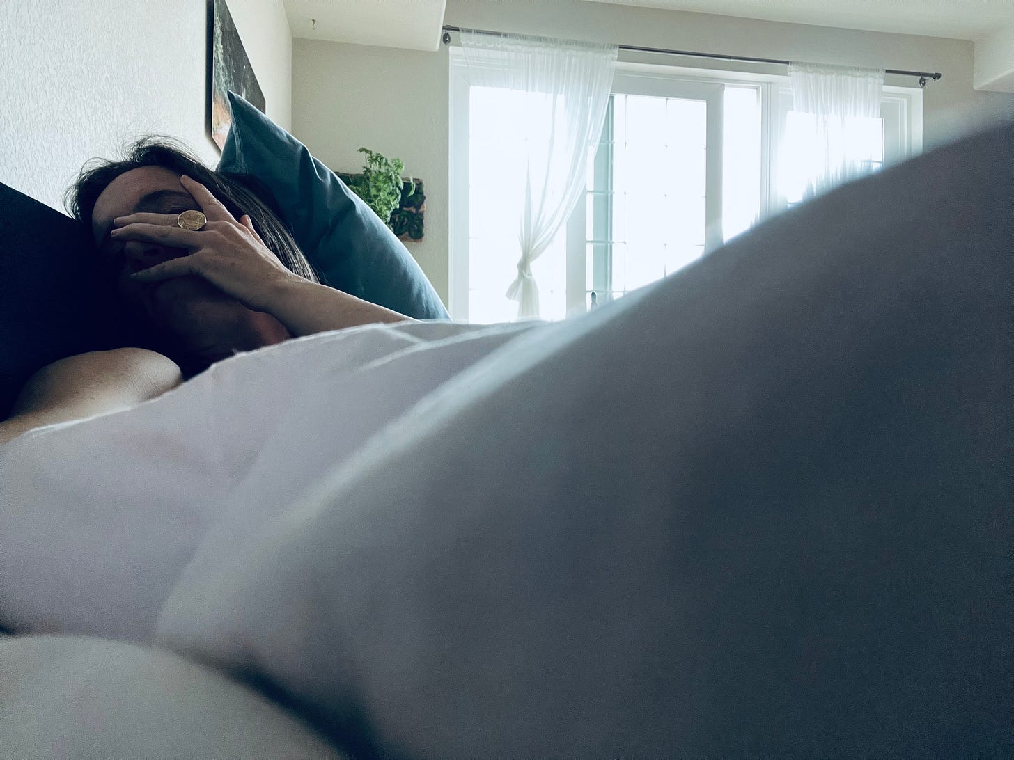 image of the author on the couch with a white down blanket over her. Her hand rests over her face.