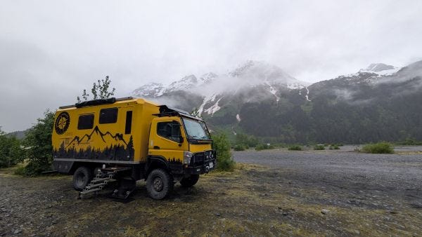 a big yellow adventure truck in front of shrouded snowy mountain peaks