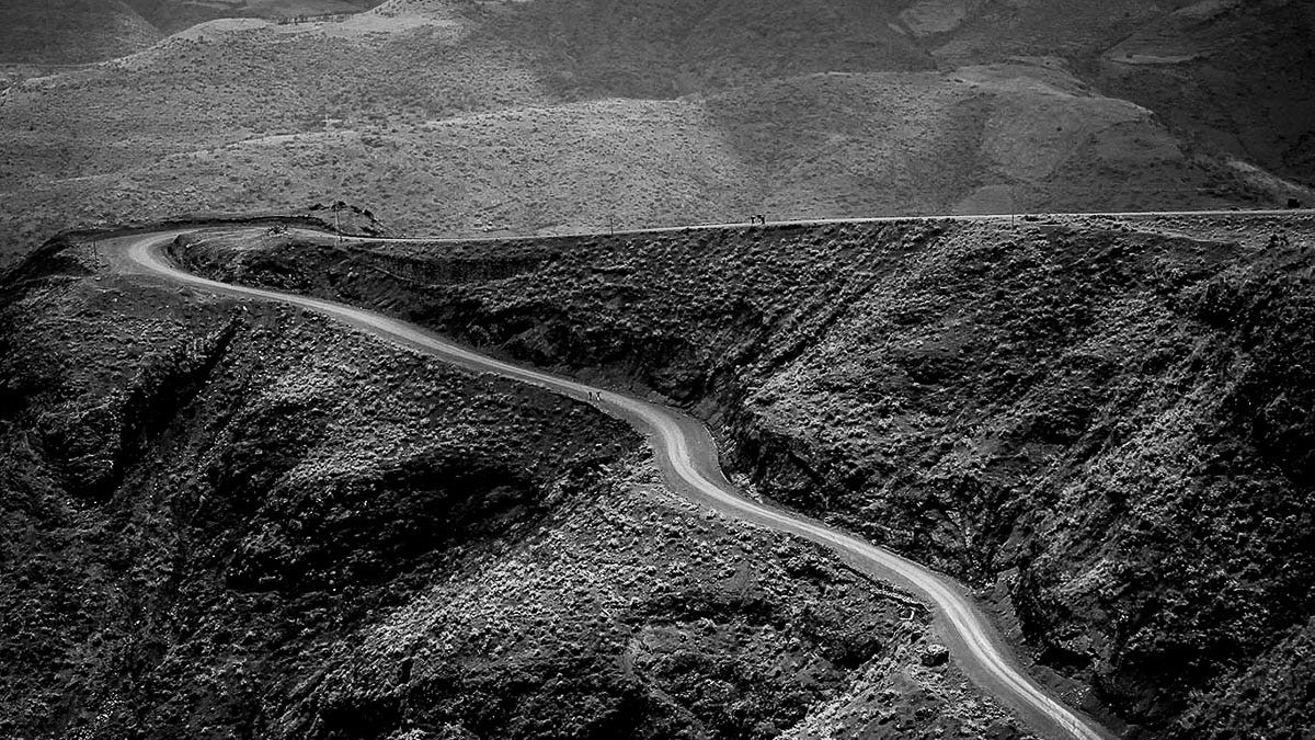 Grayscale landscape photograph of a curving dirt road carved into the steep, textured mountainside of the Simien Mountains in Ethiopia. Grayscale landscape photograph of a curving dirt road carved into the steep, textured mountainside of the Simien Mountains in Ethiopia.