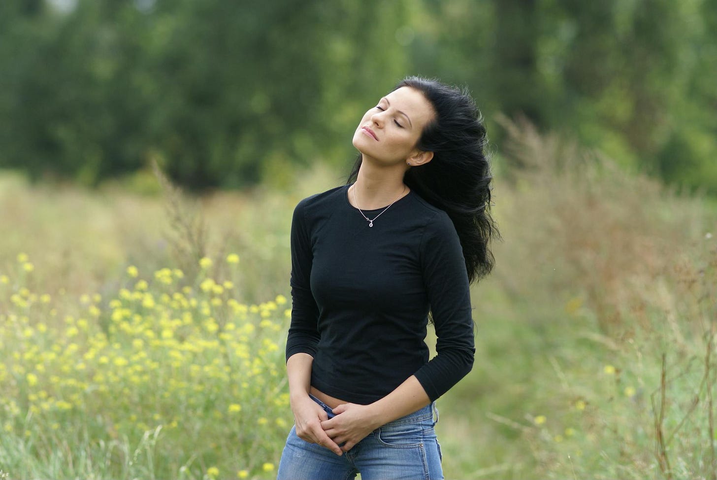 A young woman stands in a field with her eyes closed, soaking in the peace.