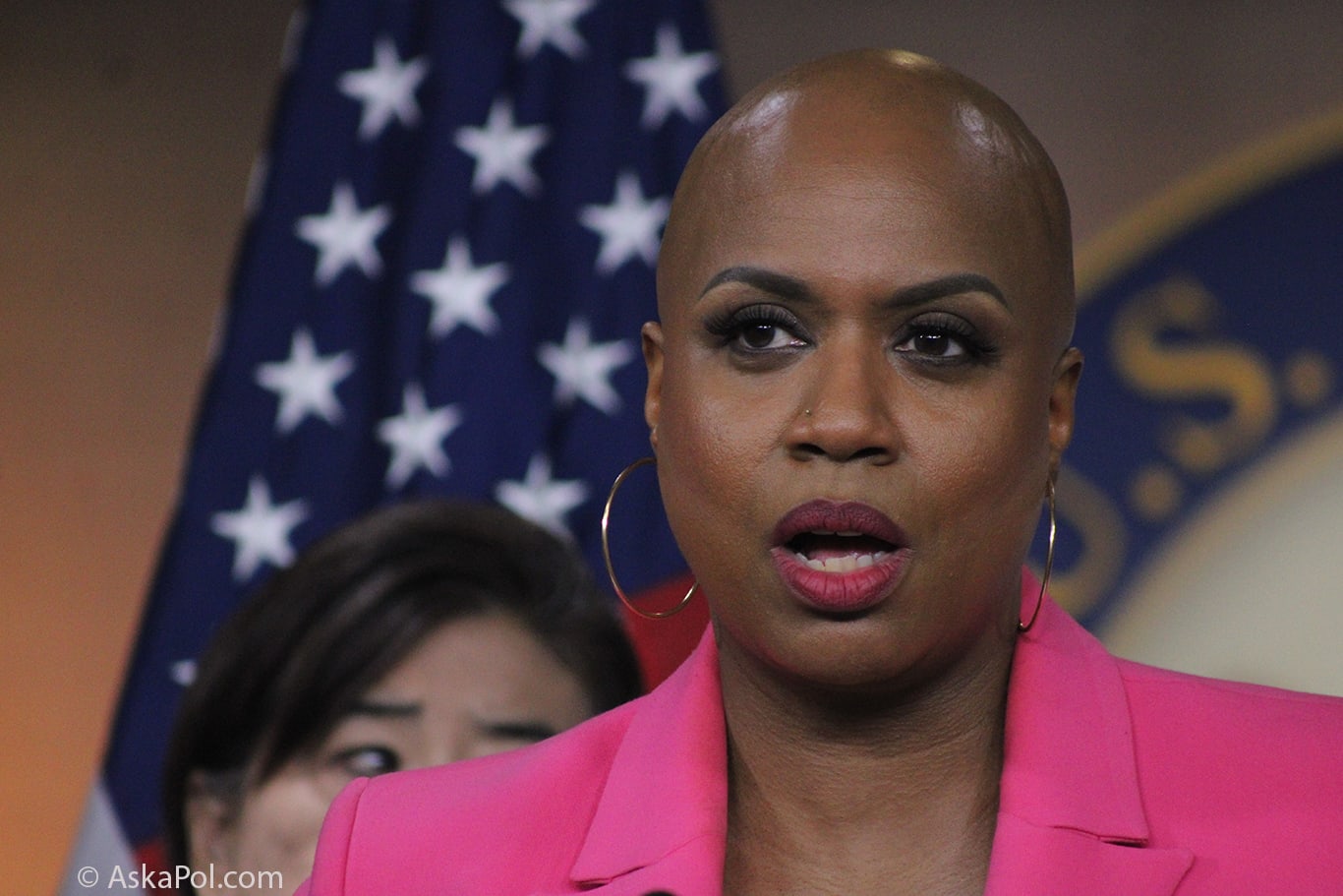 A bald black lady in a pink blazer speaks with American flag in background Photo: AskaPolpolitics.com A bald black lady in a pink blazer speaks with American flag in background Photo: AskaPolpolitics.com