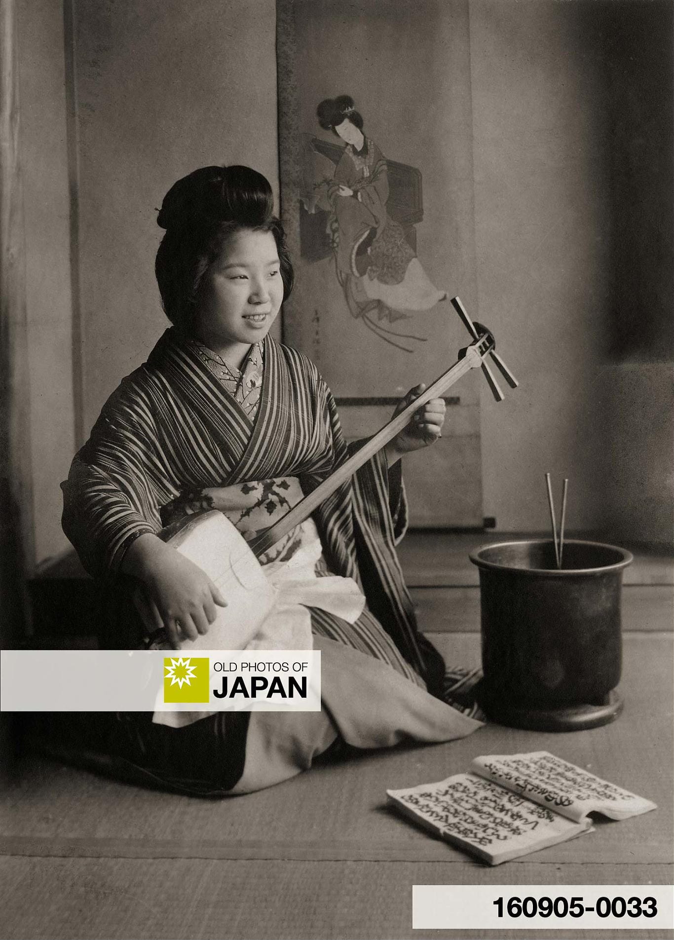 A Japanese woman plays the shamisen while seated next to a hibachi