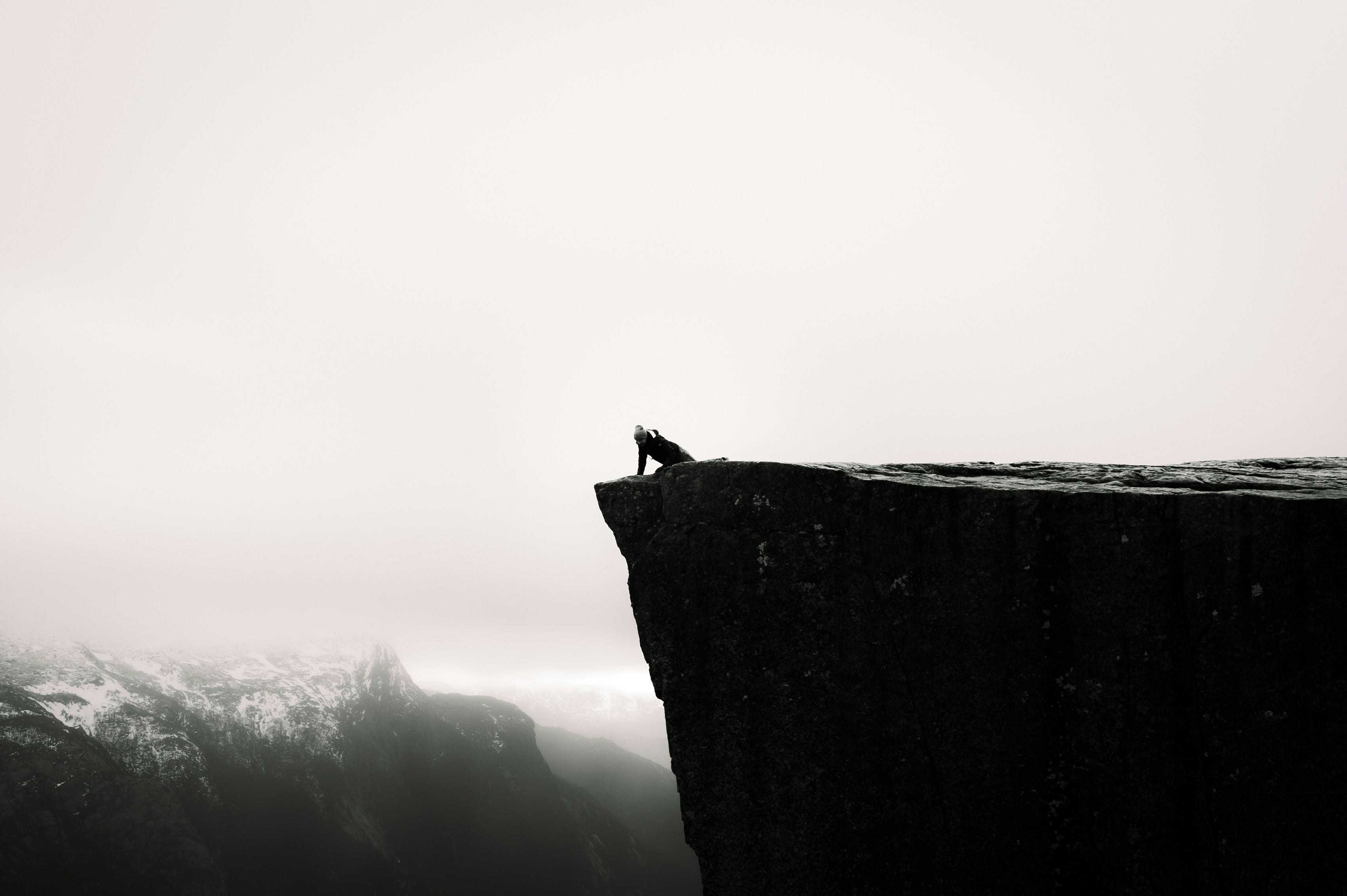 Man on hands and knees looking over a cliff into the abyss - photo from unsplash +