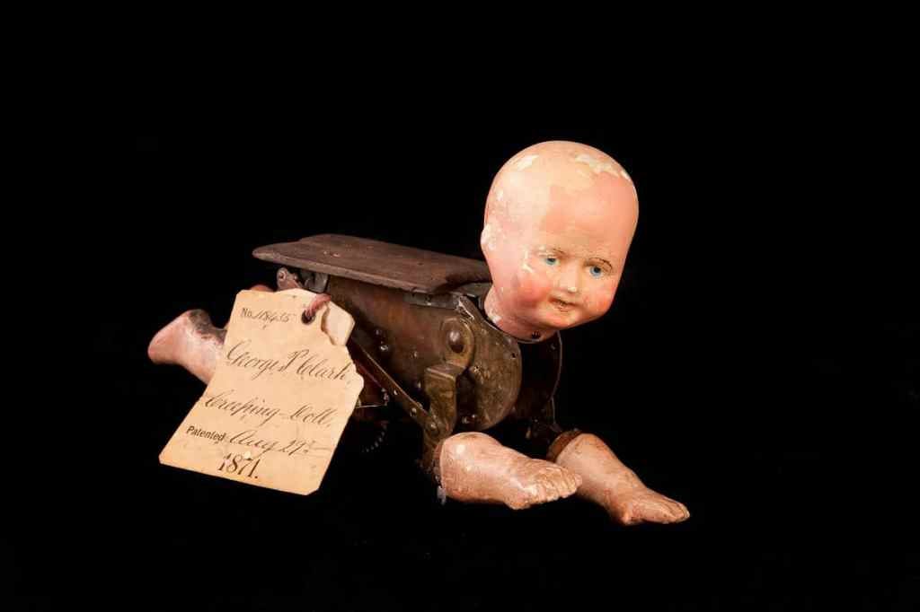 Photograph with black background of crawling white baby doll with realistic head and limbs and wooden mechanical body Photograph with black background of crawling white baby doll with realistic head and limbs and wooden mechanical body