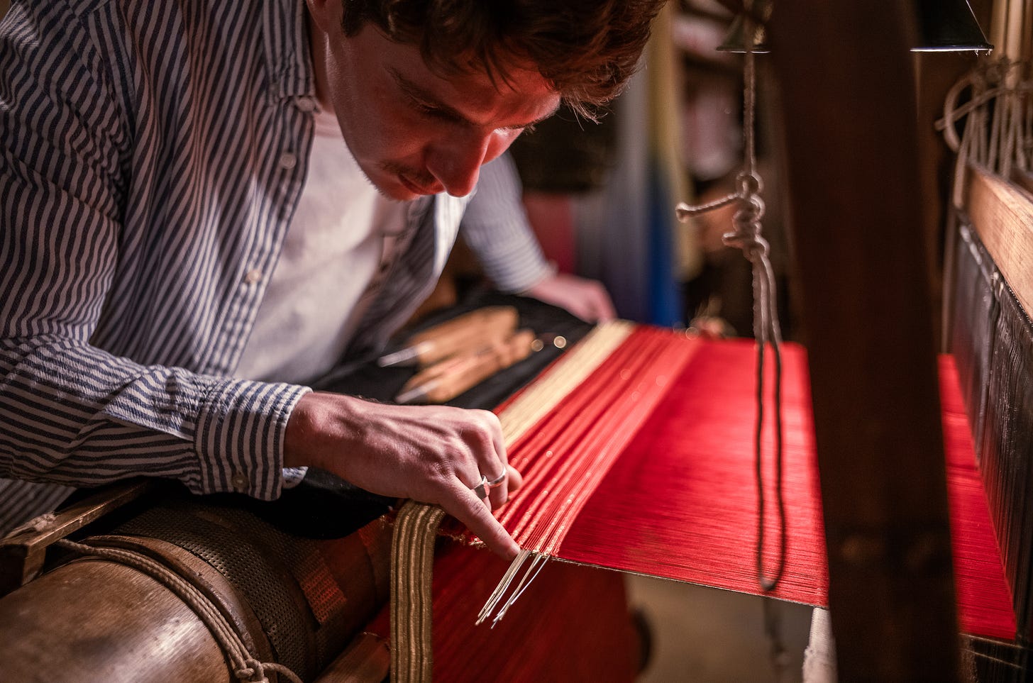 Virgile De la Calle carefully weaving bright red threads on a traditional loom