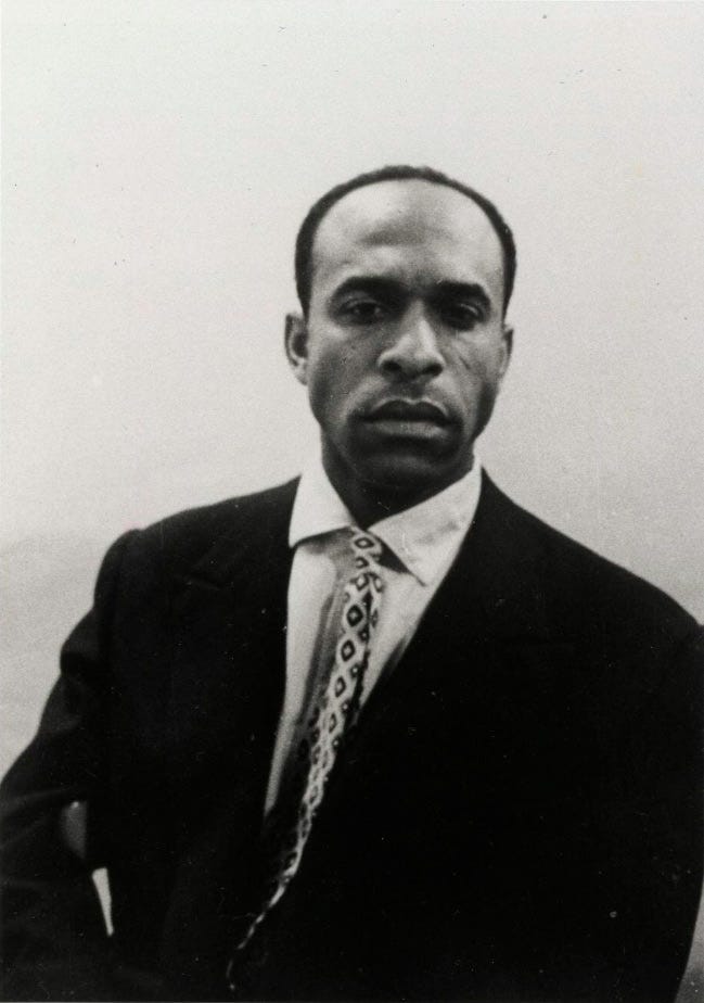 Um retrato em preto e branco de Frantz Fanon, um homem negro de cabelos curtos usando terno.