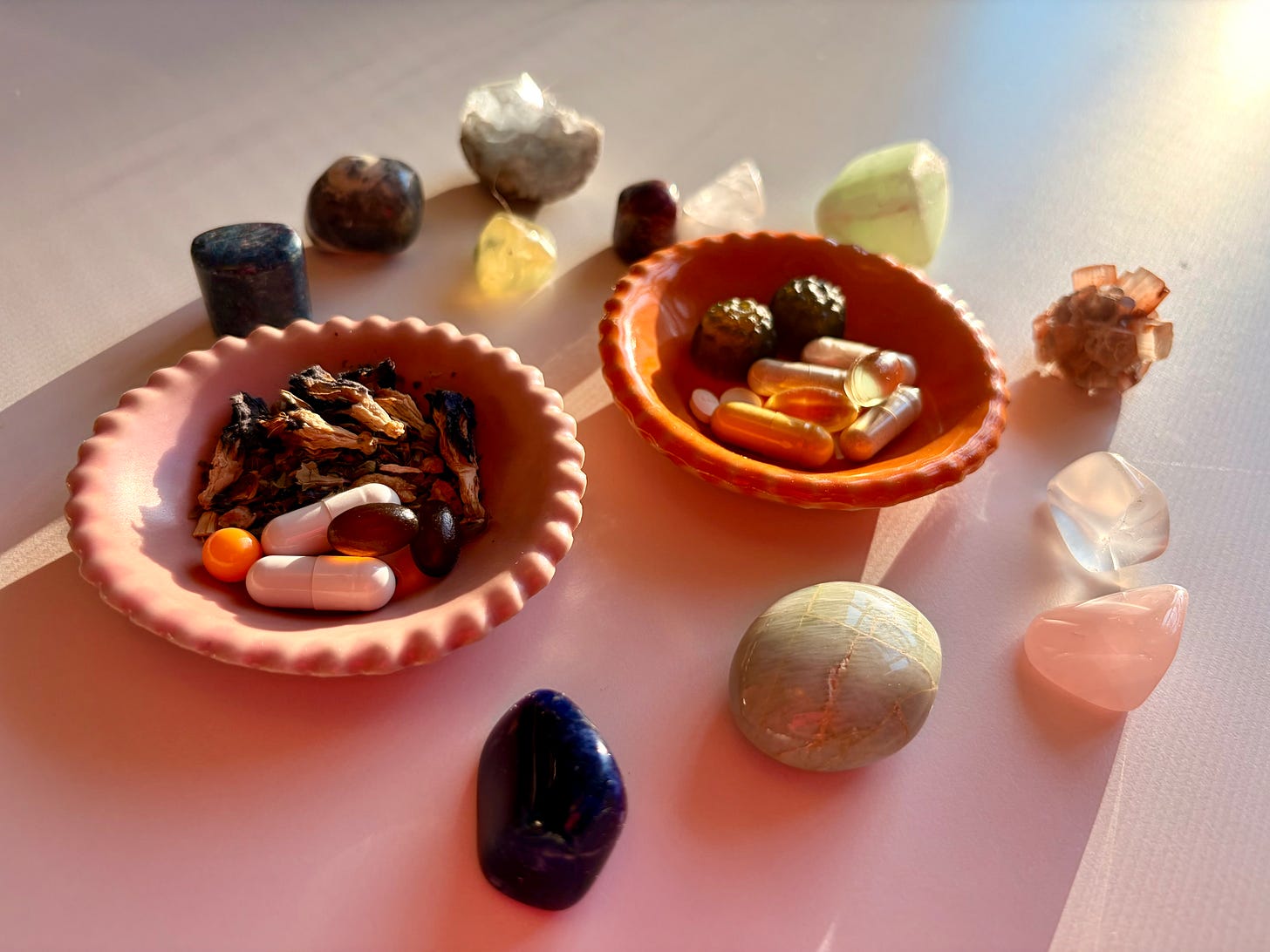 An image of supplements, tea leaves, and small crystals, bathed in pink and orange hues.